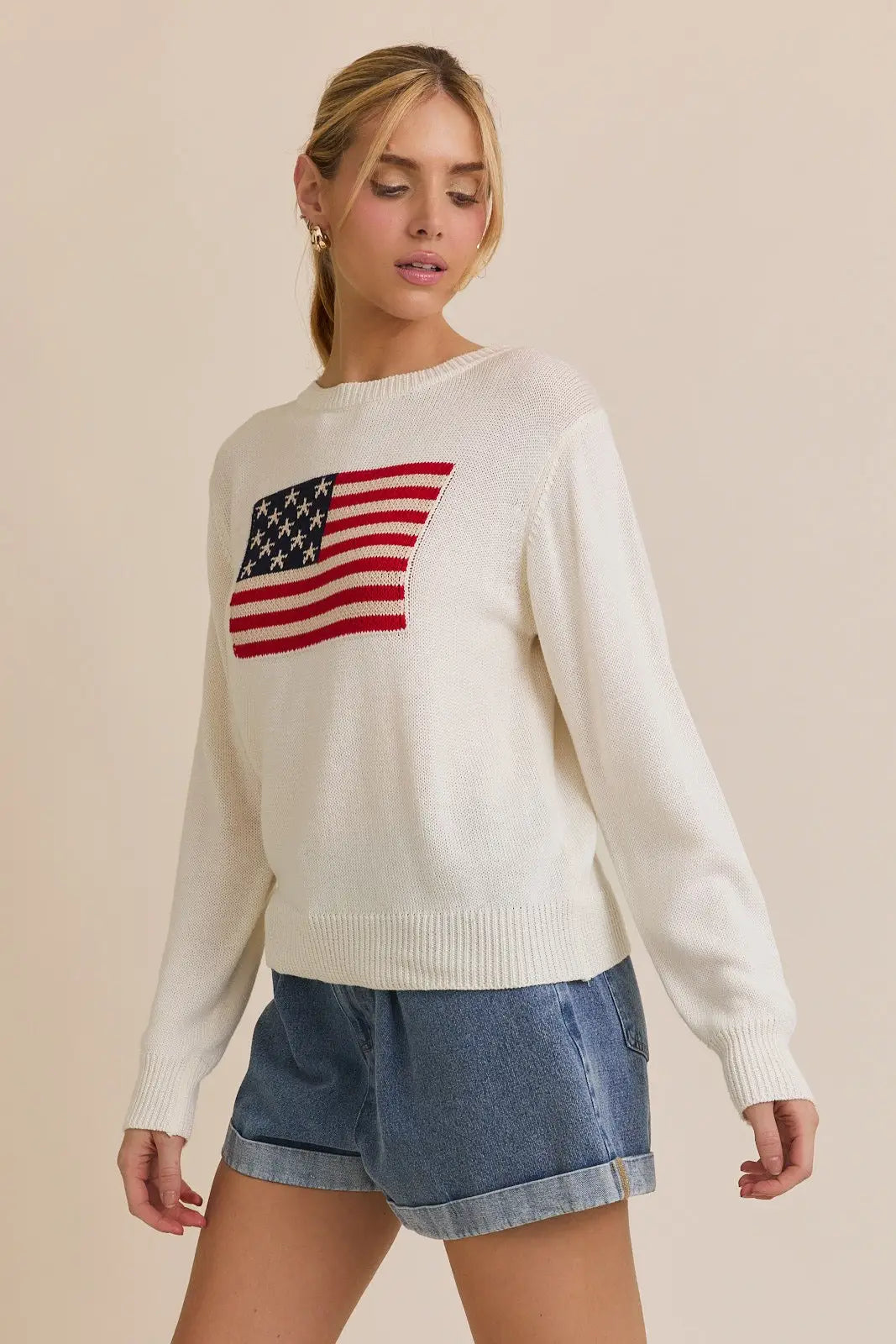 Woman wearing a white American flag round neck sweater top featuring a patriotic design