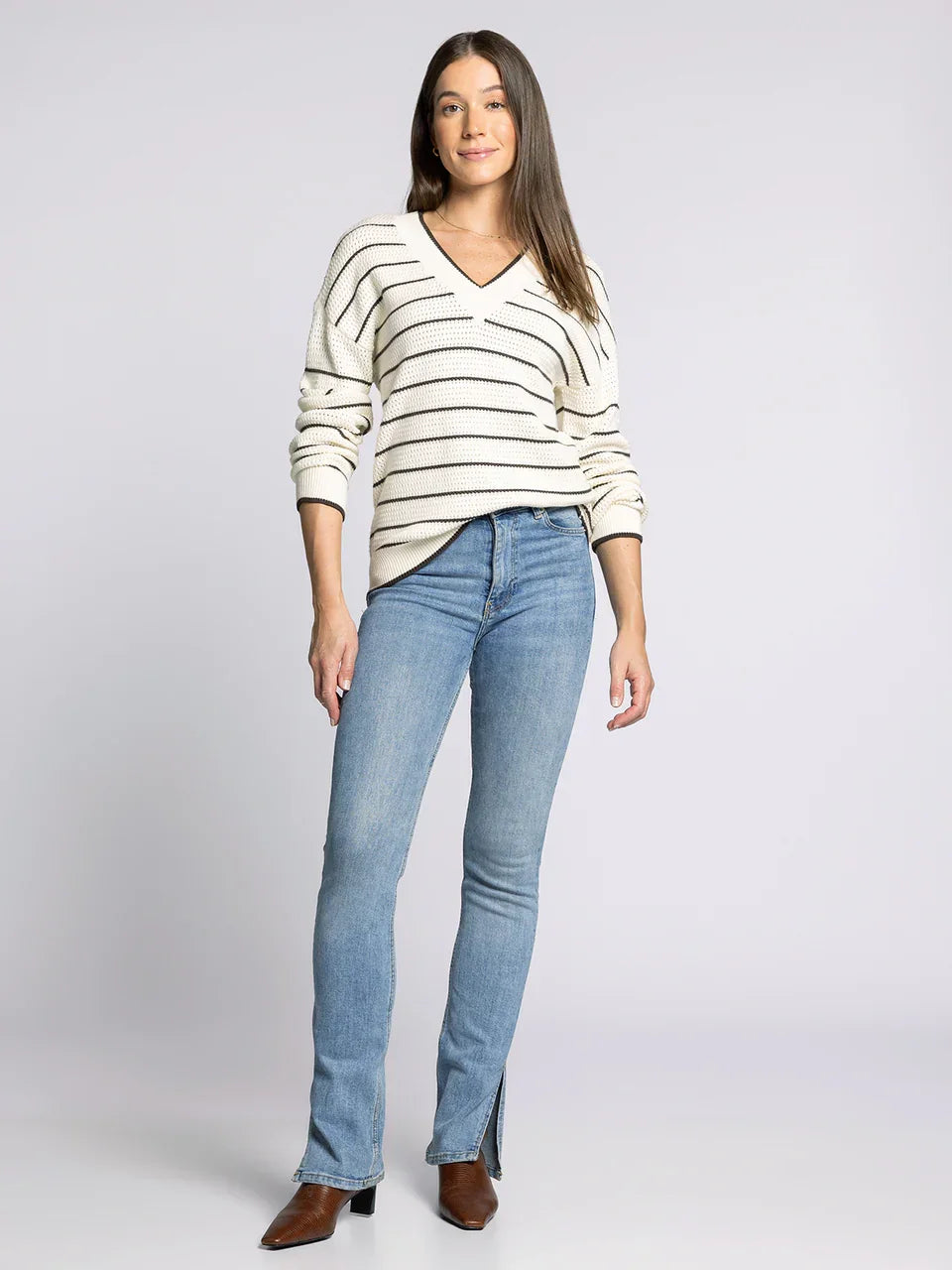 Women’s cream and black striped V-neck IRA sweater with light blue slim-fit jeans and brown heeled boots