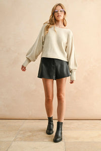 Women’s cream boat neck sweater with black faux leather shorts and ankle boots