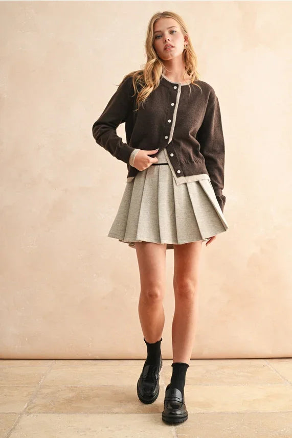 Women’s dark brown cardigan with light trim and pleated mini skirt, featuring color contrast button