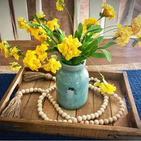 Yellow daffodils in a turquoise mason jar complemented by wooden beads and rustic decor