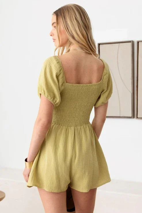 Yellow boho romper with short sleeves and smocked bodice worn by a woman