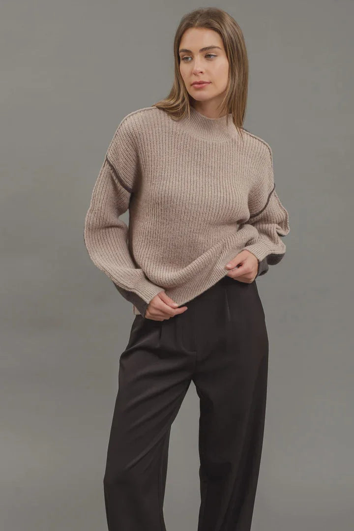 Young woman in beige ribbed colorblock mock neck knit sweater and dark trousers