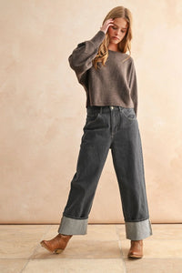 Young woman wearing a brown boat neck sweater with dark gray wide-leg jeans and ankle boots