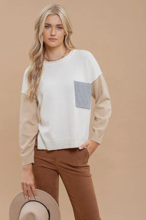 Young woman in colorblock long sleeve knit sweater and brown pants, holding a hat