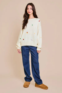 Young woman in a cream long sleeve embroidered sweater with colorful details and jeans