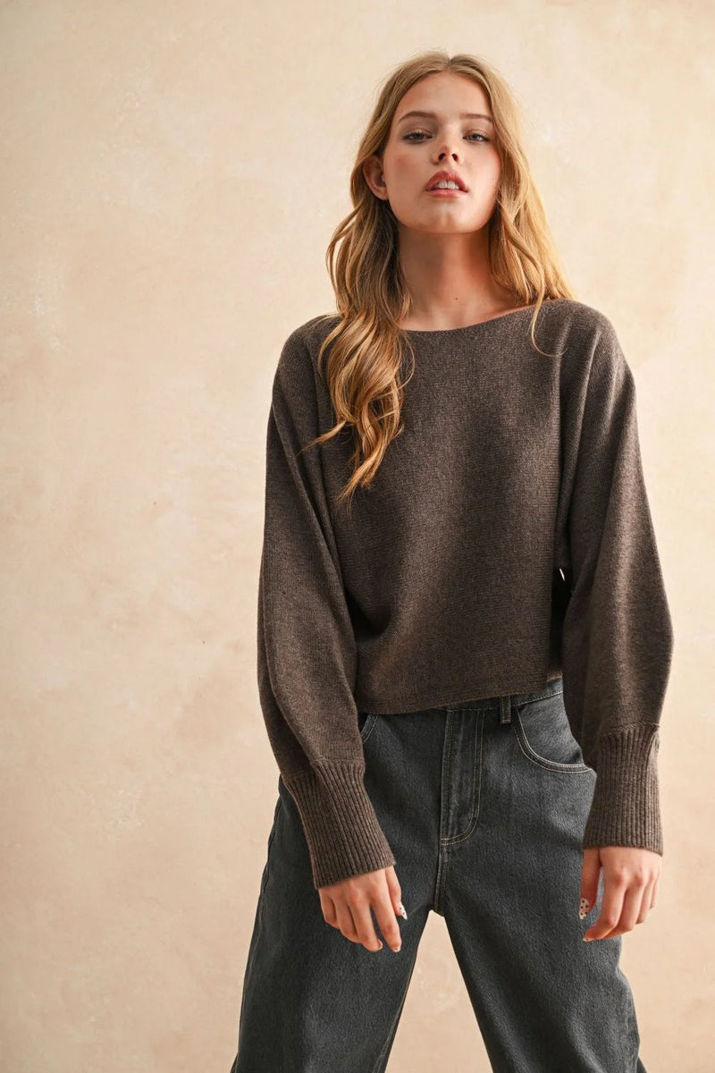 Young woman wearing a dark brown boat neck sweater and dark gray jeans