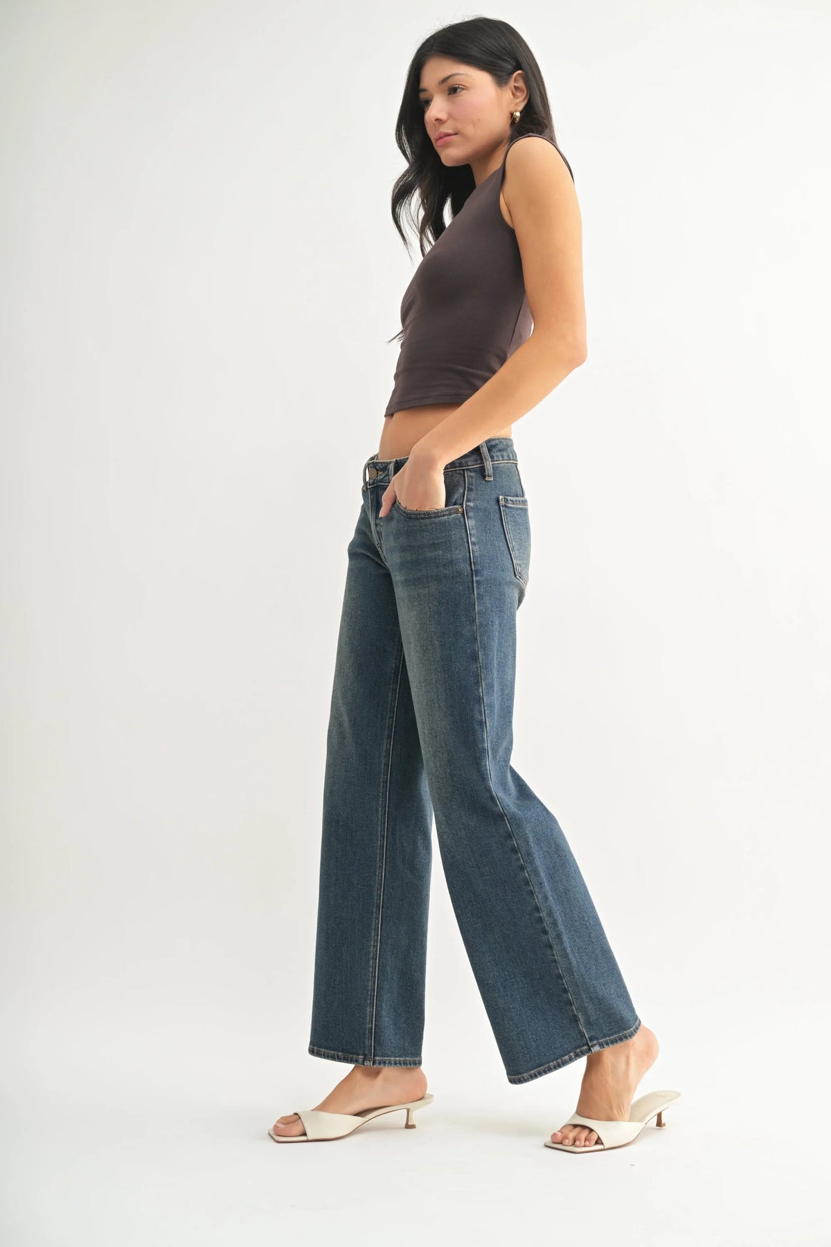 Young woman wearing low rise straight denim jeans, dark sleeveless top, and white heels