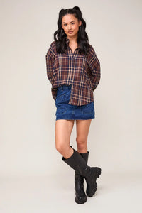 Young woman in an oversized plaid shirt, denim skirt, and black boots outfit