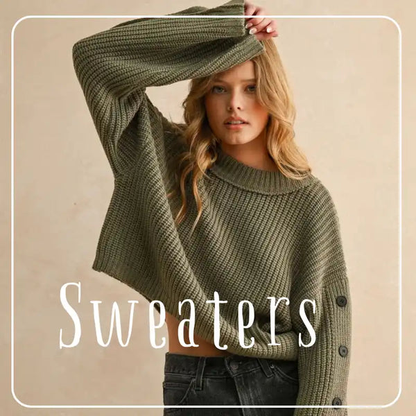 A woman modeling a loose-fitting, cropped olive green knit sweater with wide sleeves and decorative buttons on the cuffs.