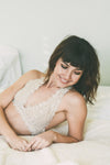 A girl laying on a bed wearing a white, lace, halter top bralette.